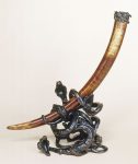 Cet objet représente une longue défense d'éléphant enchassée dans un socle de bronze représentant trois serpents de bronze entrelacés et la bouche ouverte, semblant se battre.